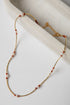 Necklace with gold chain and red and white beads on a light background