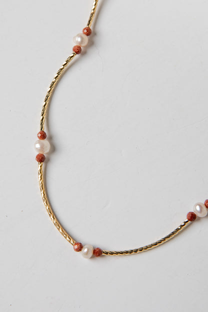 Necklace with gold chain and red and white beads on a light gray background