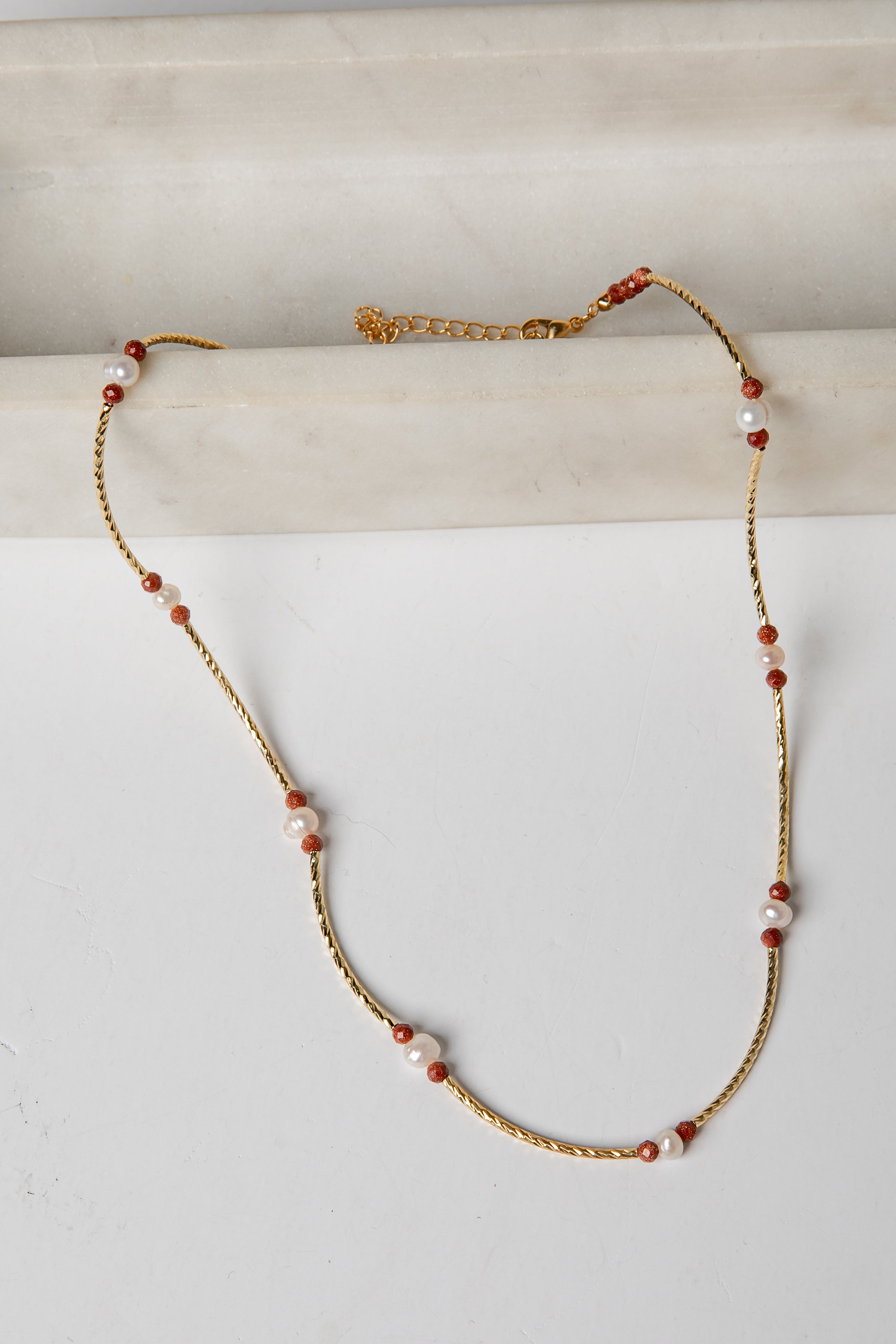 Necklace with gold chain and red and white beads on a light background