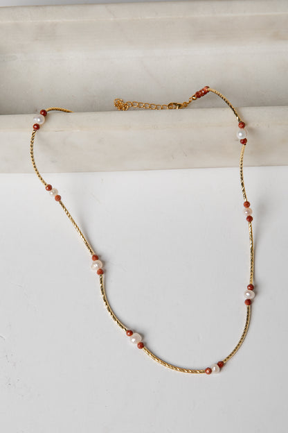 Necklace with gold chain and red and white beads on a light background