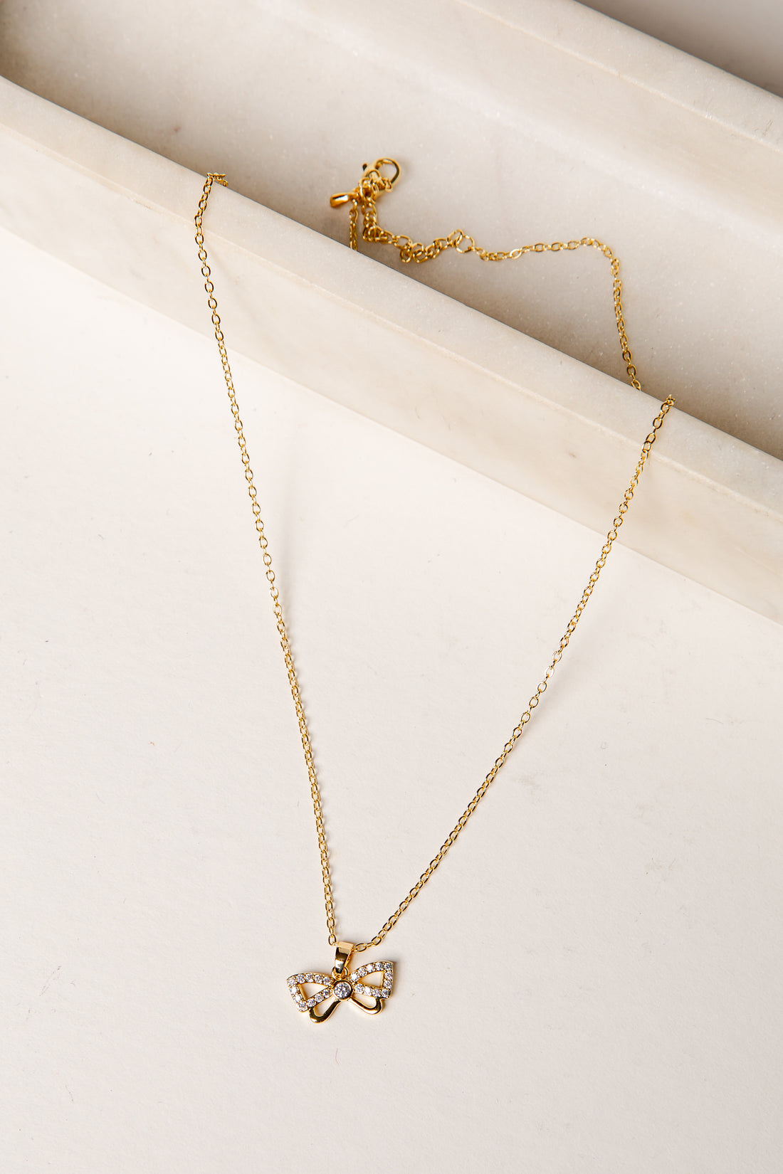 Gold necklace with a bow pendant on a light beige surface