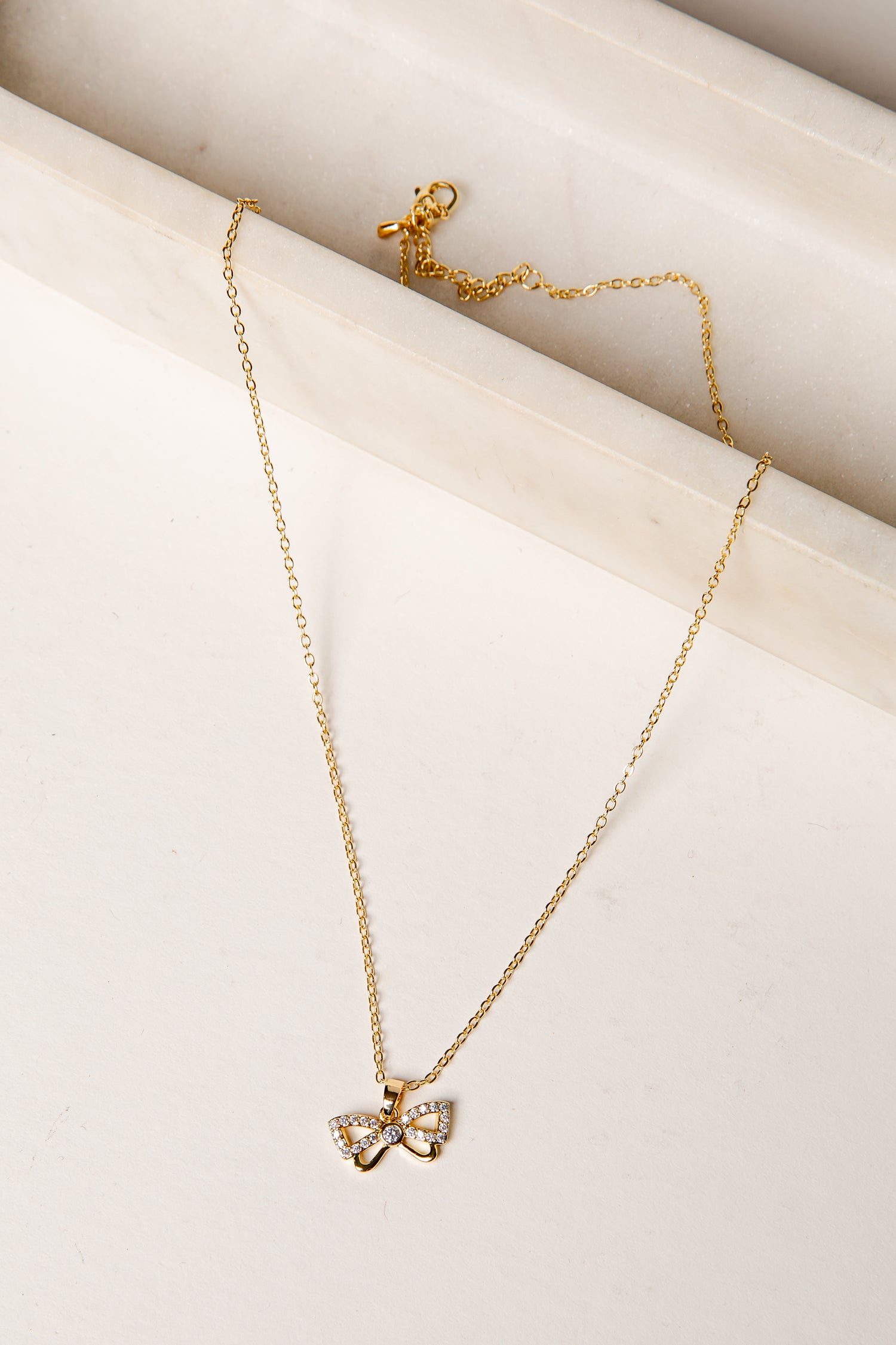 Gold necklace with a bow pendant on a light beige surface