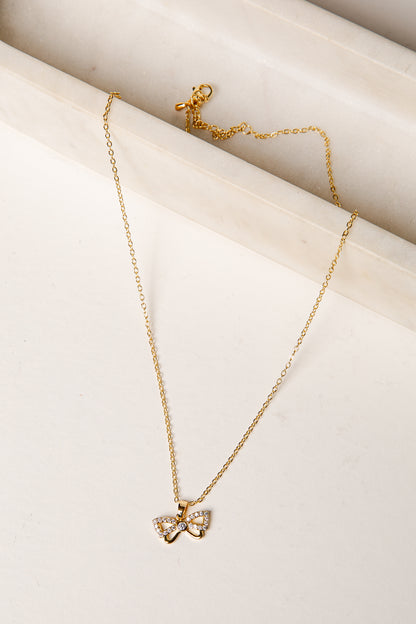 Gold necklace with a bow pendant on a light beige surface