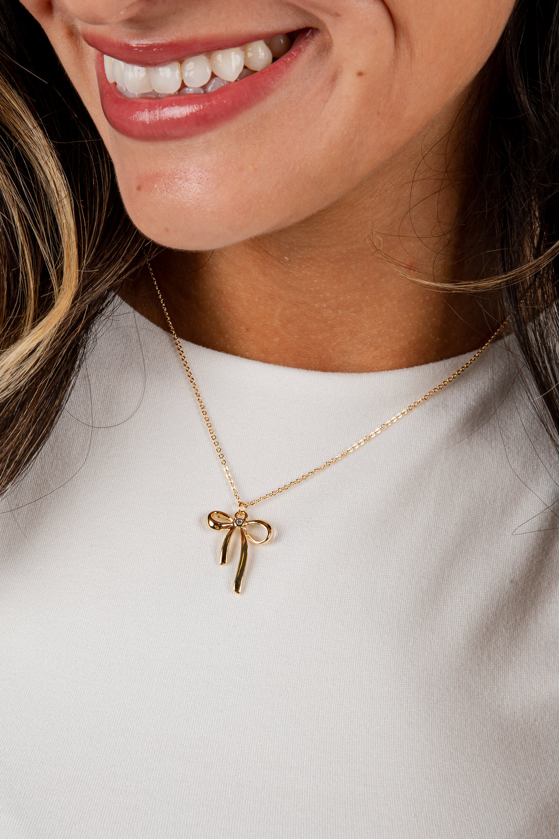Close-up of a person wearing a gold bow-shaped necklace on a plain background