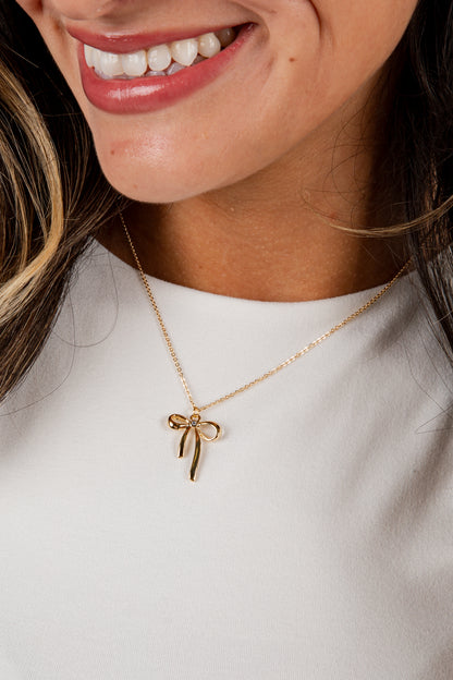 Close-up of a person wearing a gold bow-shaped necklace on a plain background