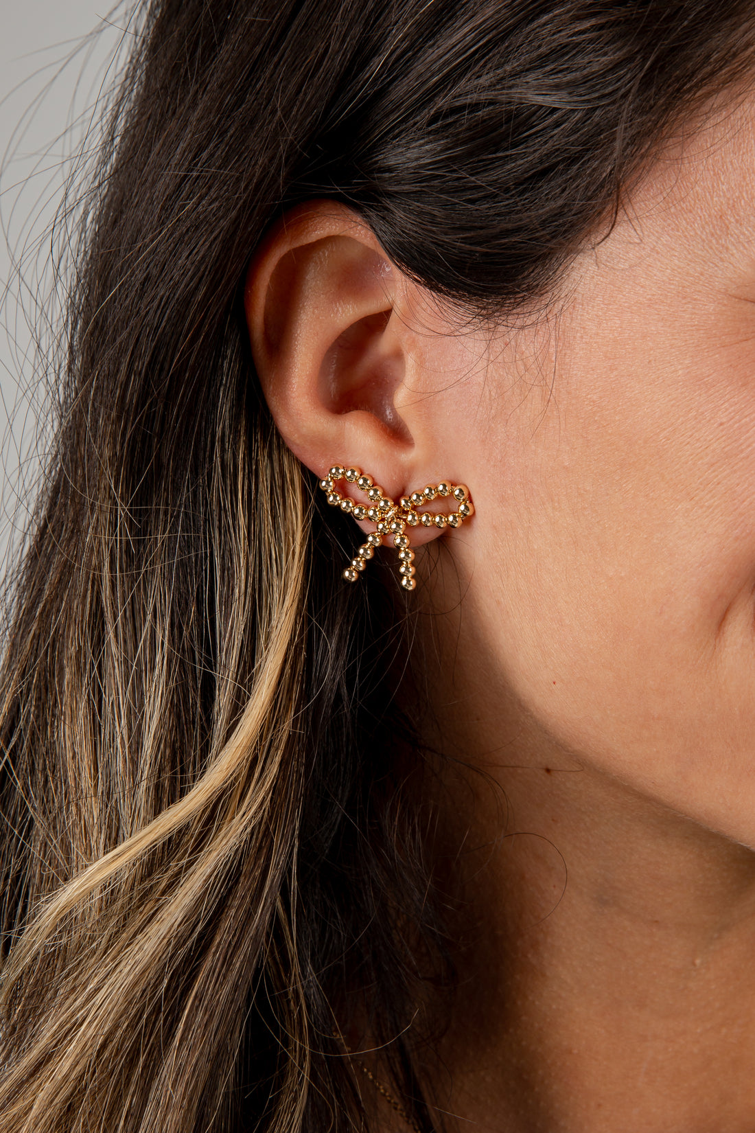 Close-up of an ear wearing a gold bow-shaped earring with a blurred background