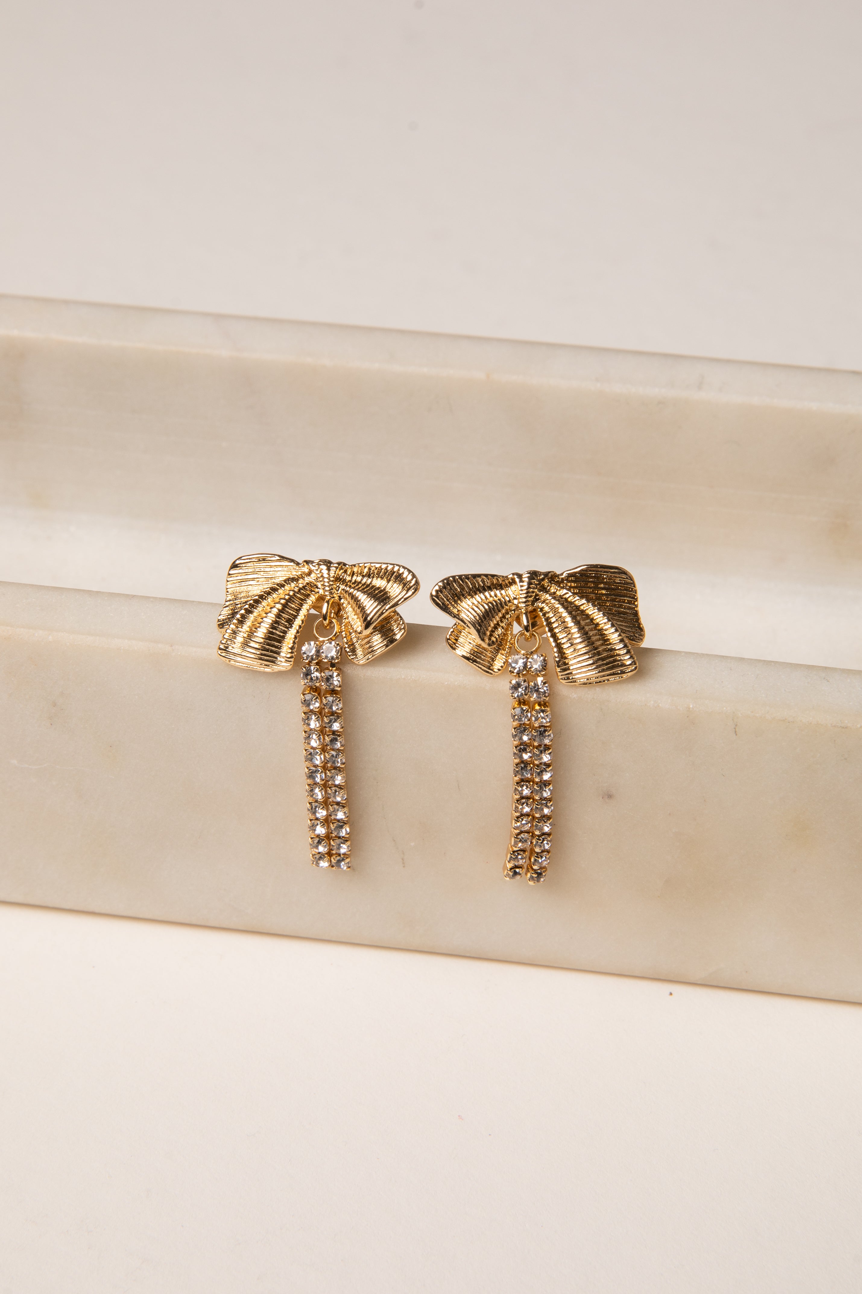 Gold earrings with tassel design on a beige surface