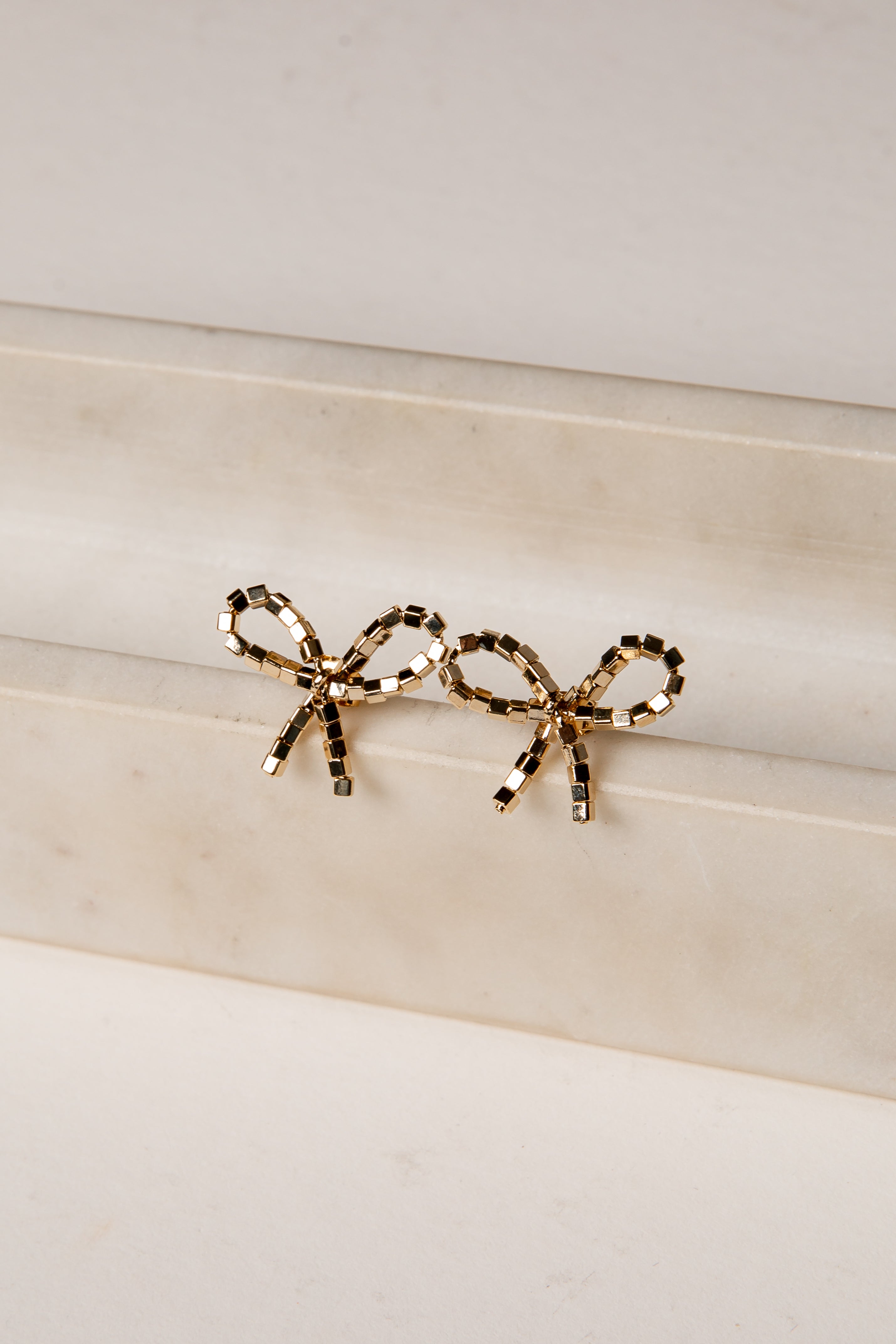 Gold bow-shaped earrings on a marble surface