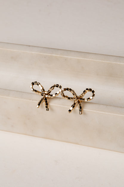 Gold bow-shaped earrings on a marble surface