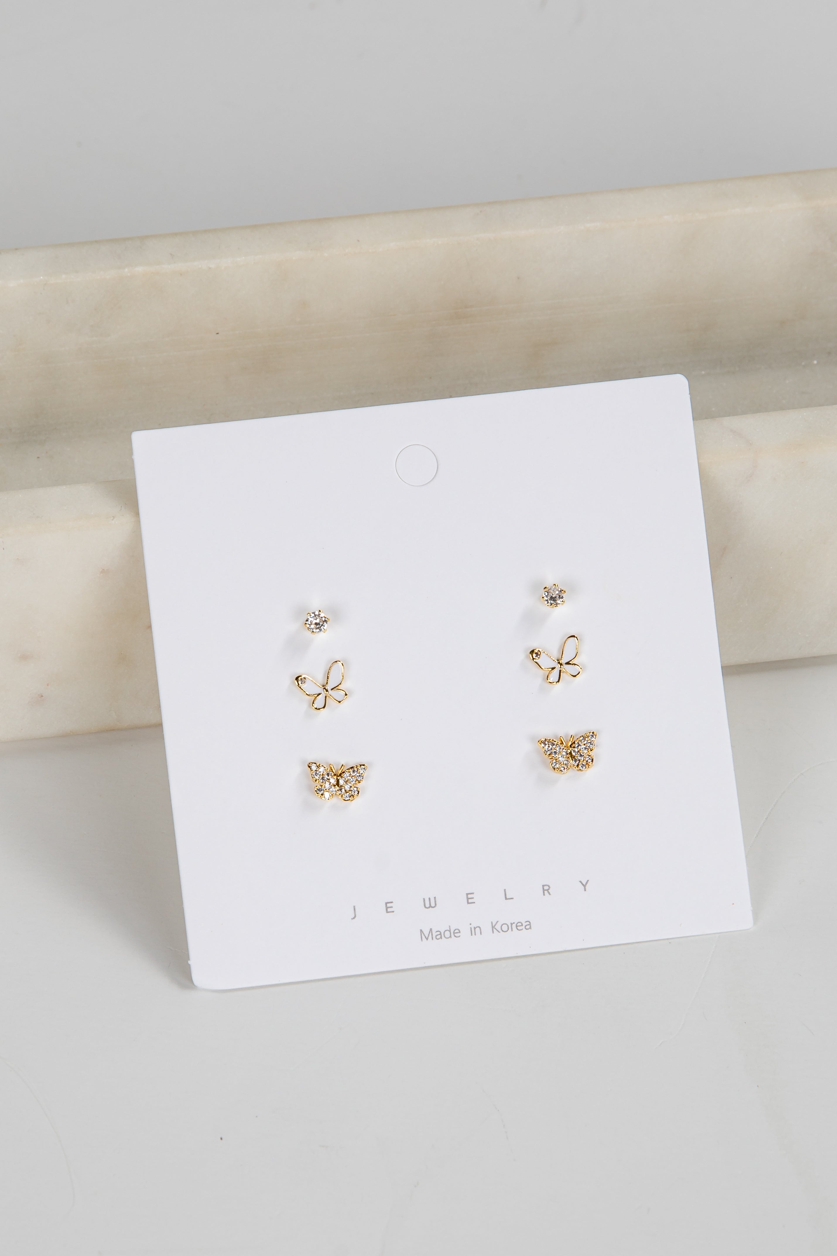 Set of gold butterfly earrings on a white jewelry card with a marble surface background