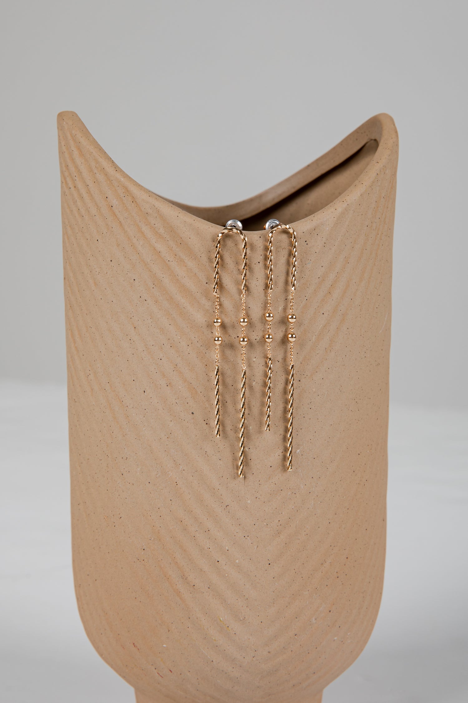 Gold chain earrings on a beige stand against a gray background