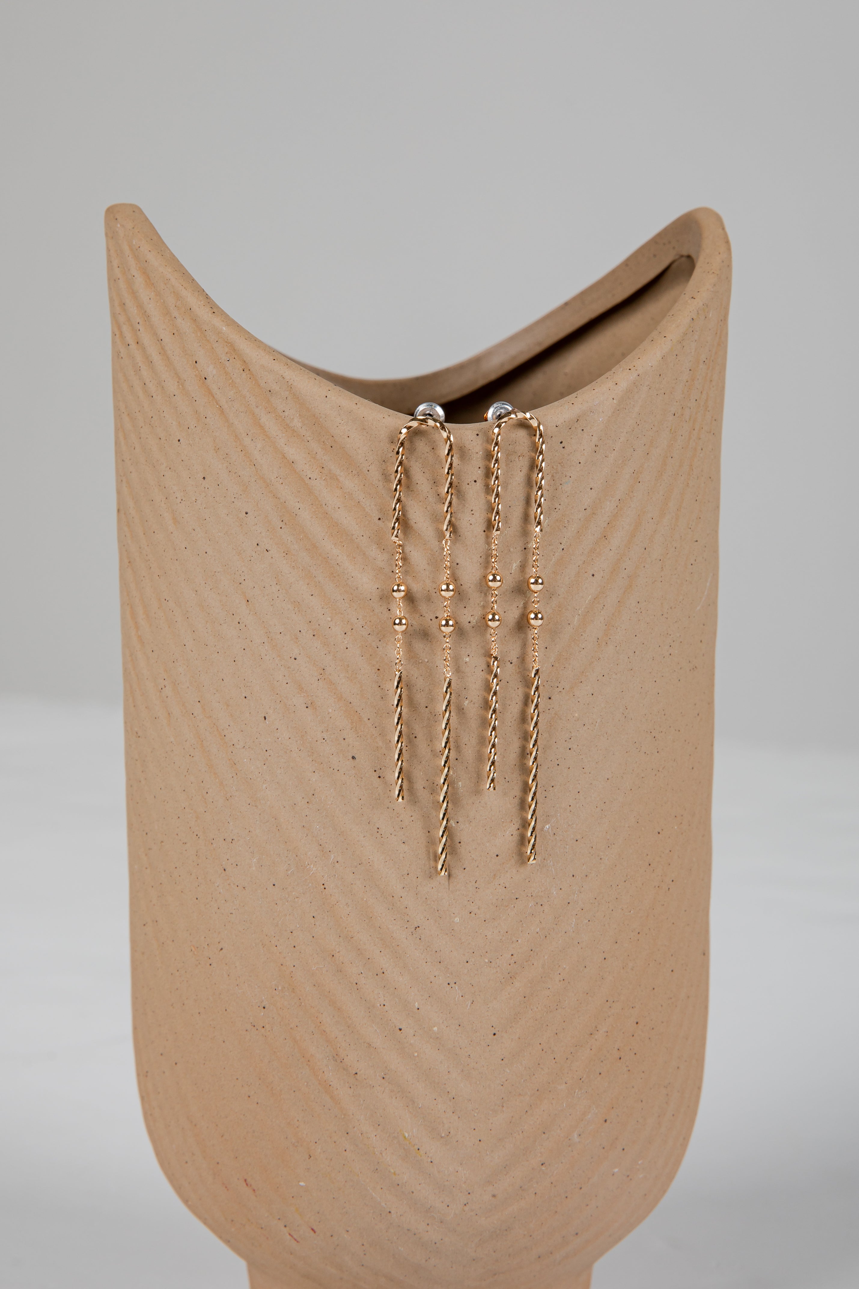 Gold chain earrings on a beige stand against a gray background