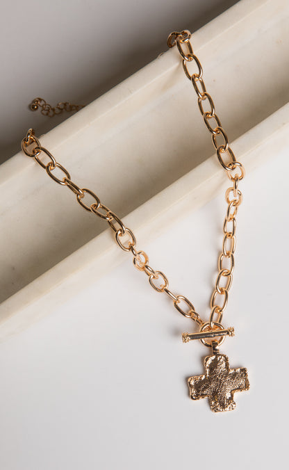 Gold chain necklace with a cross pendant on a white surface