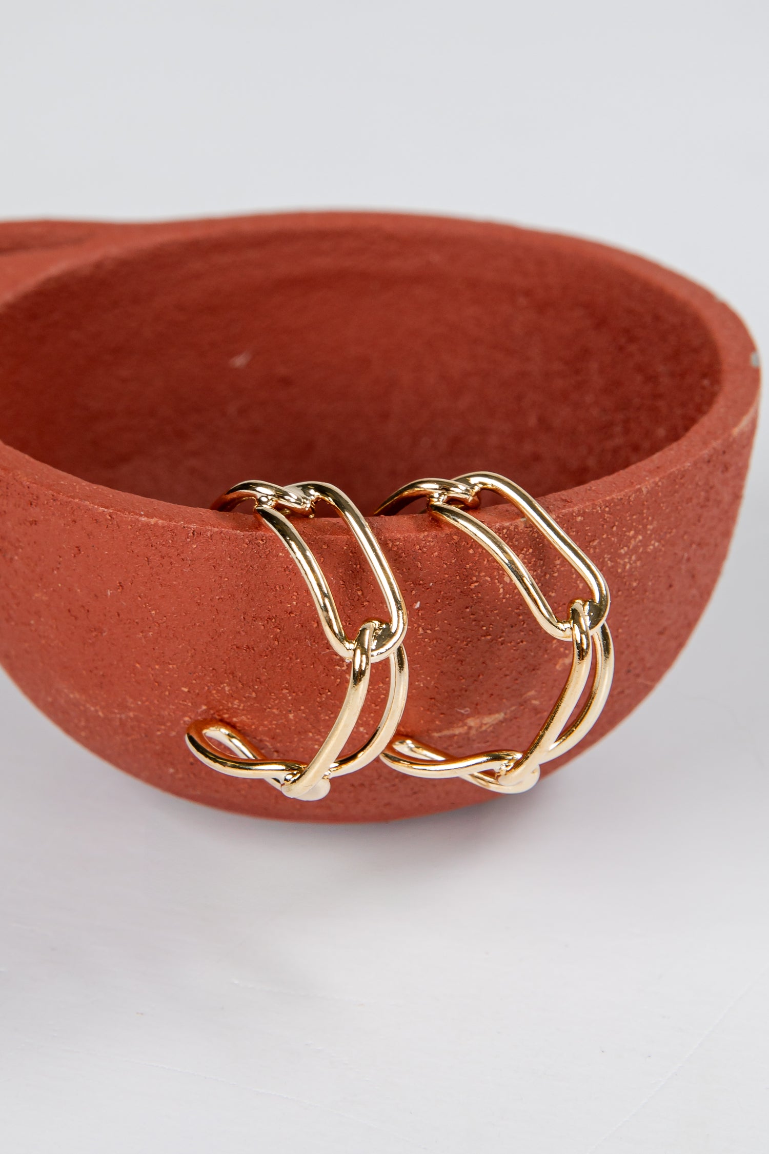 Three gold hoop earrings on a terracotta dish against a white background