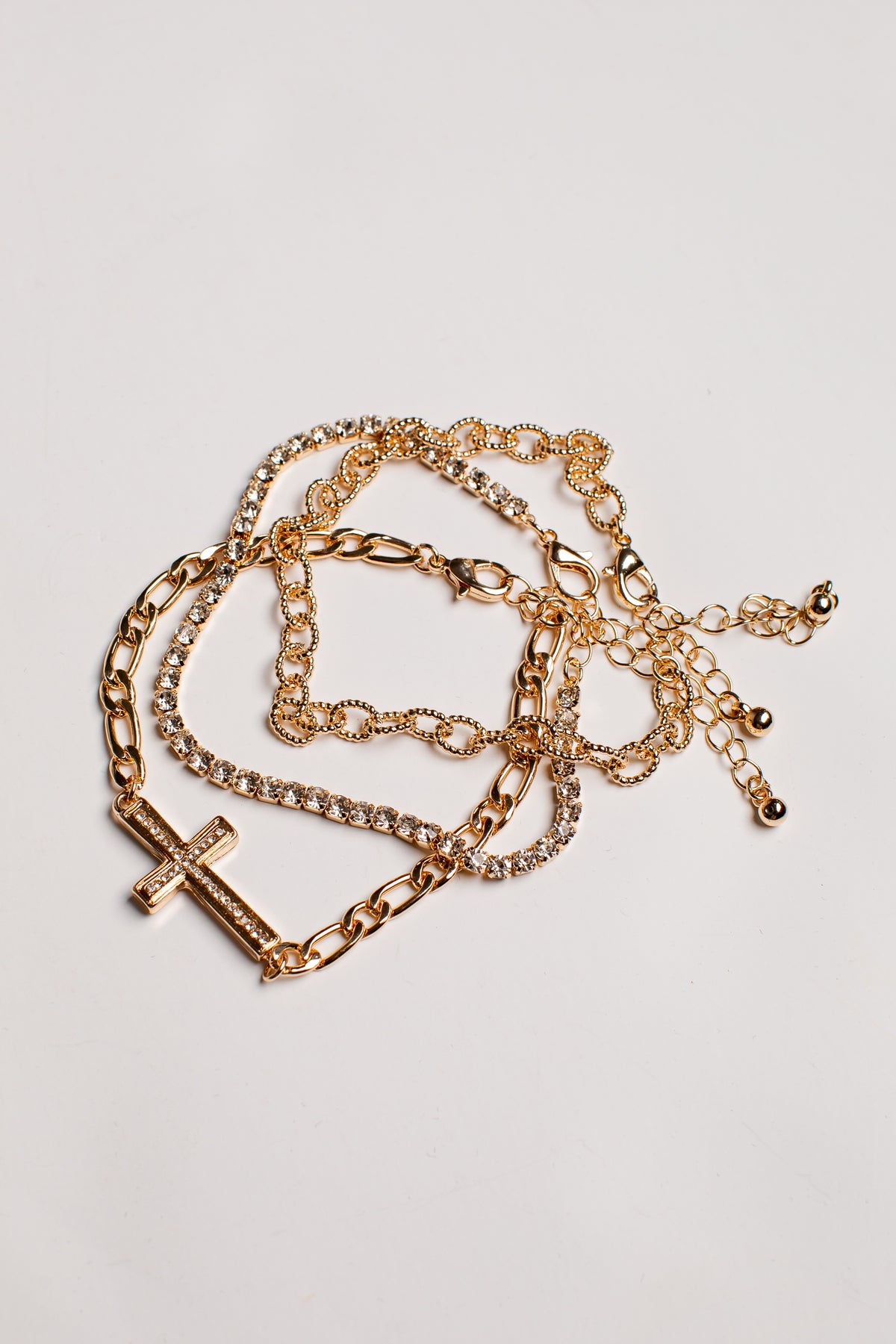 A gold-toned multi-strand chain bracelet featuring a cross pendant with engraved text, displayed on a light gray background.