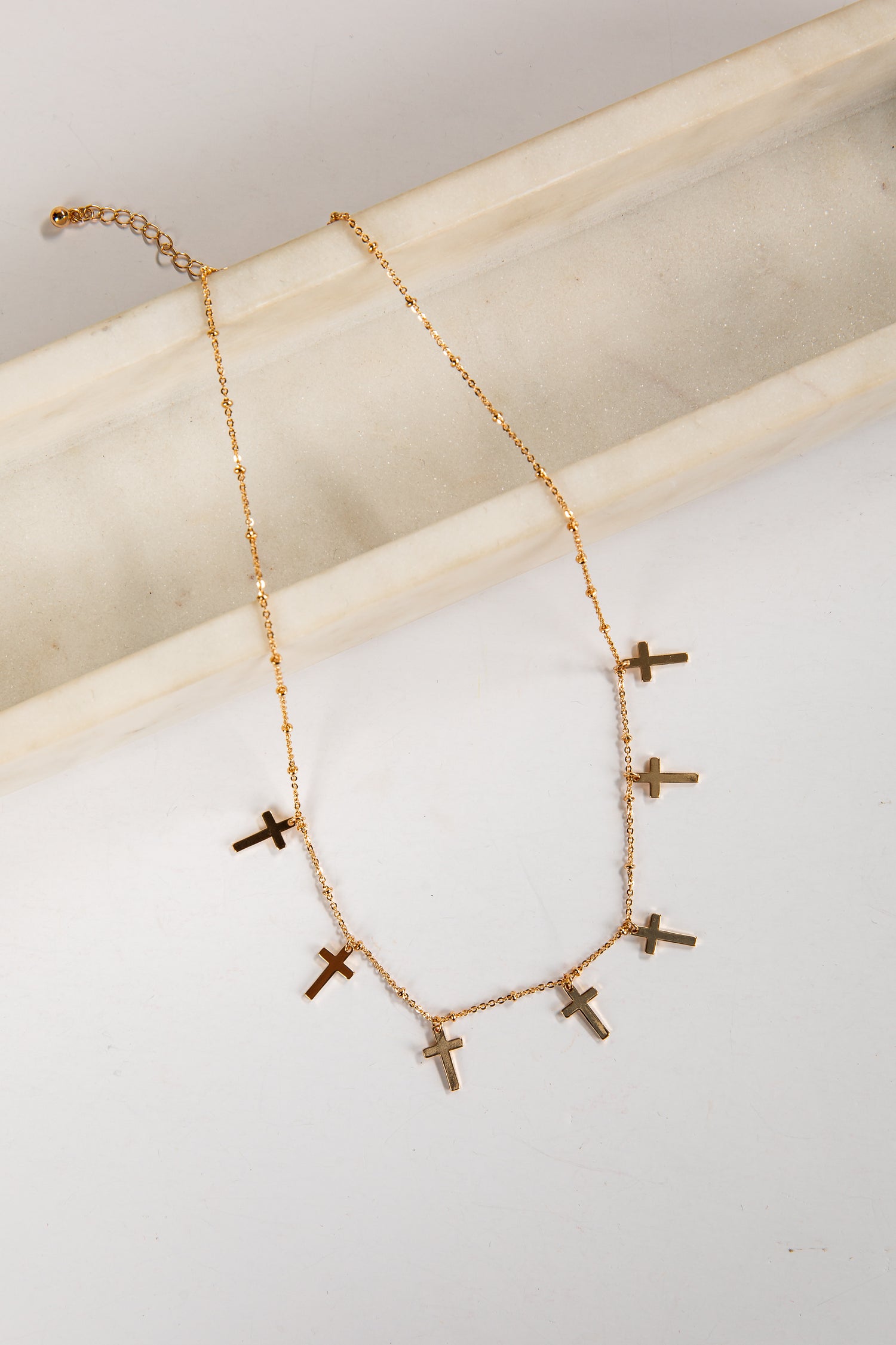 Gold necklace with small crosses on a light background