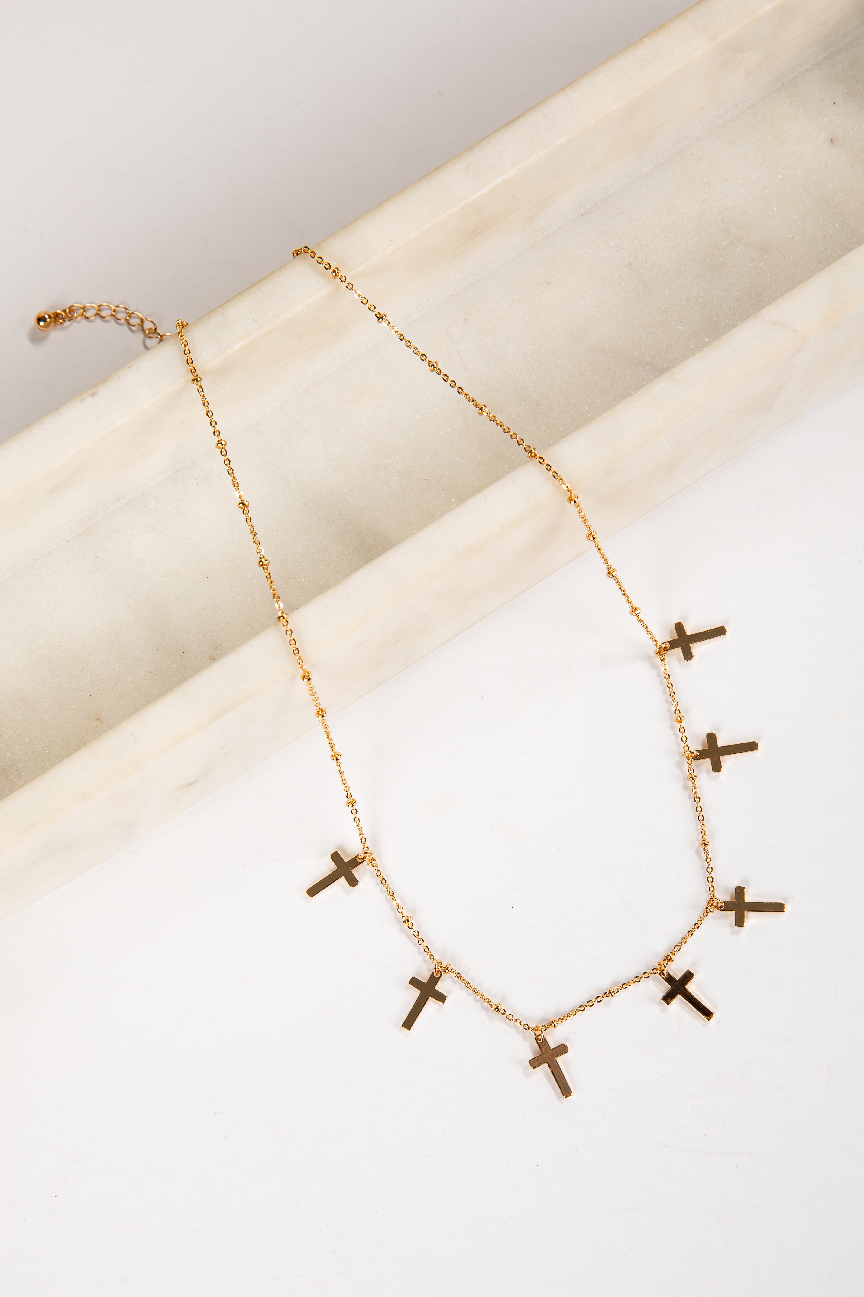 Gold necklace with small crosses on a white surface