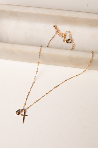 Gold necklace with a cross pendant on a light wooden surface