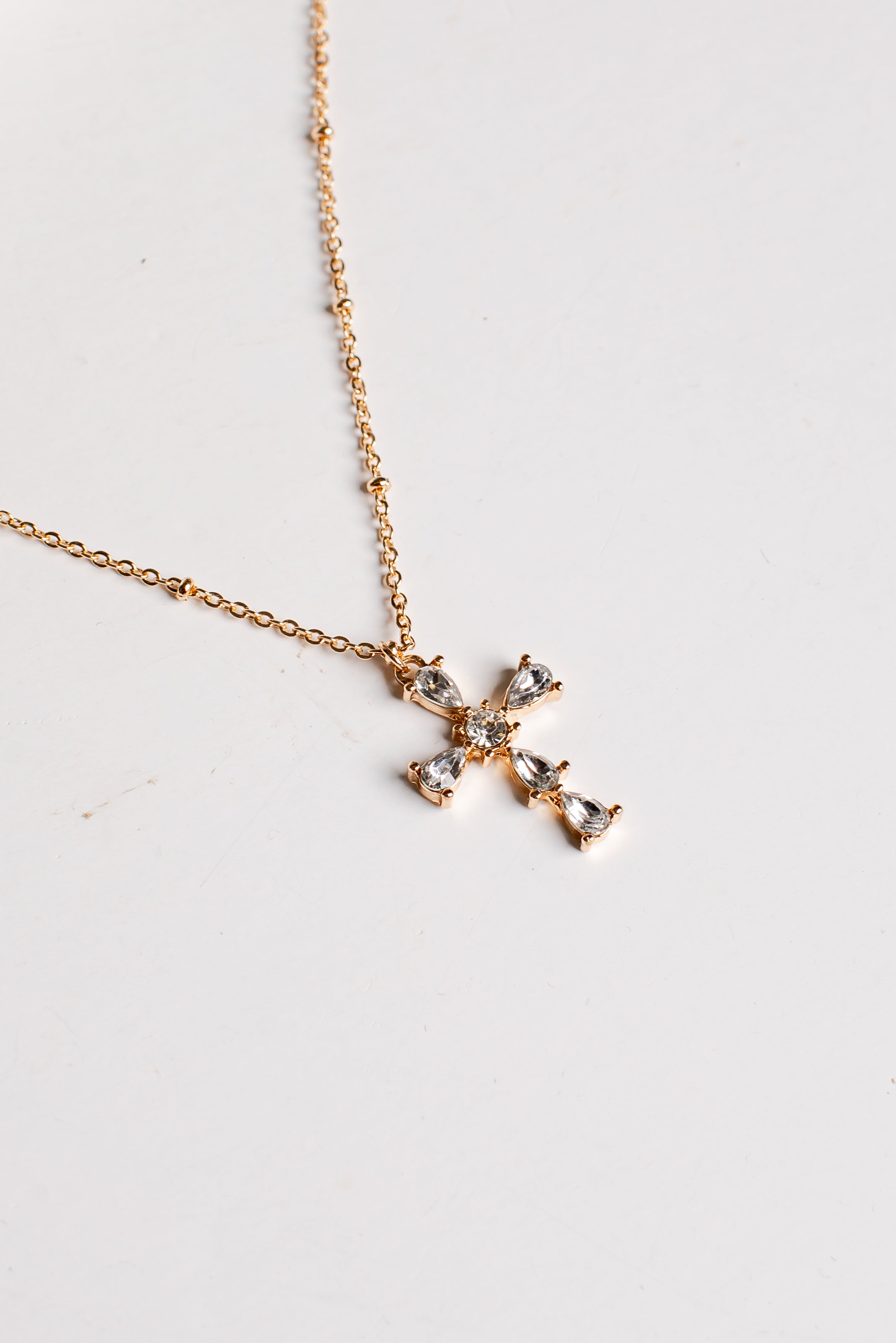 A delicate gold chain necklace with a small cross pendant adorned with clear crystals, displayed on a plain white surface.