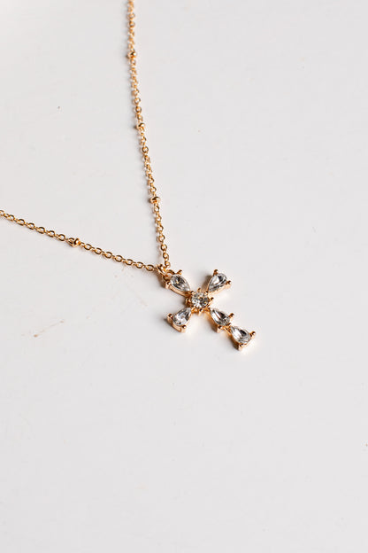 A delicate gold chain necklace with a small cross pendant adorned with clear crystals, displayed on a plain white surface.