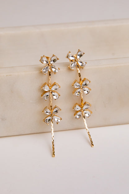 Gold rhinestone floral earrings on a beige surface
