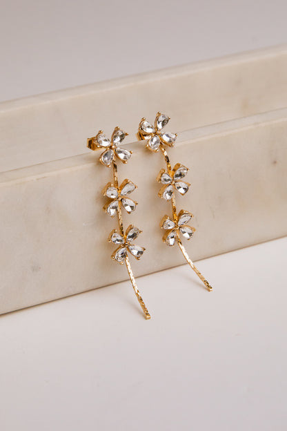 Gold floral earrings on a light wooden surface