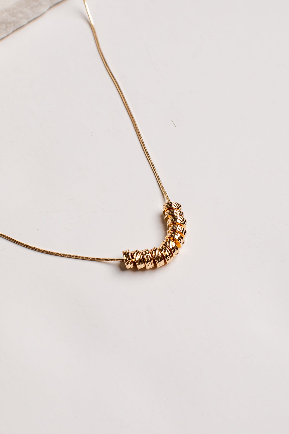 A delicate gold chain necklace featuring a curved segment of faceted, textured gold beads, photographed on a clean off-white surface.