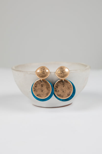 Gold earrings with blue accents on a white dish against a light gray background