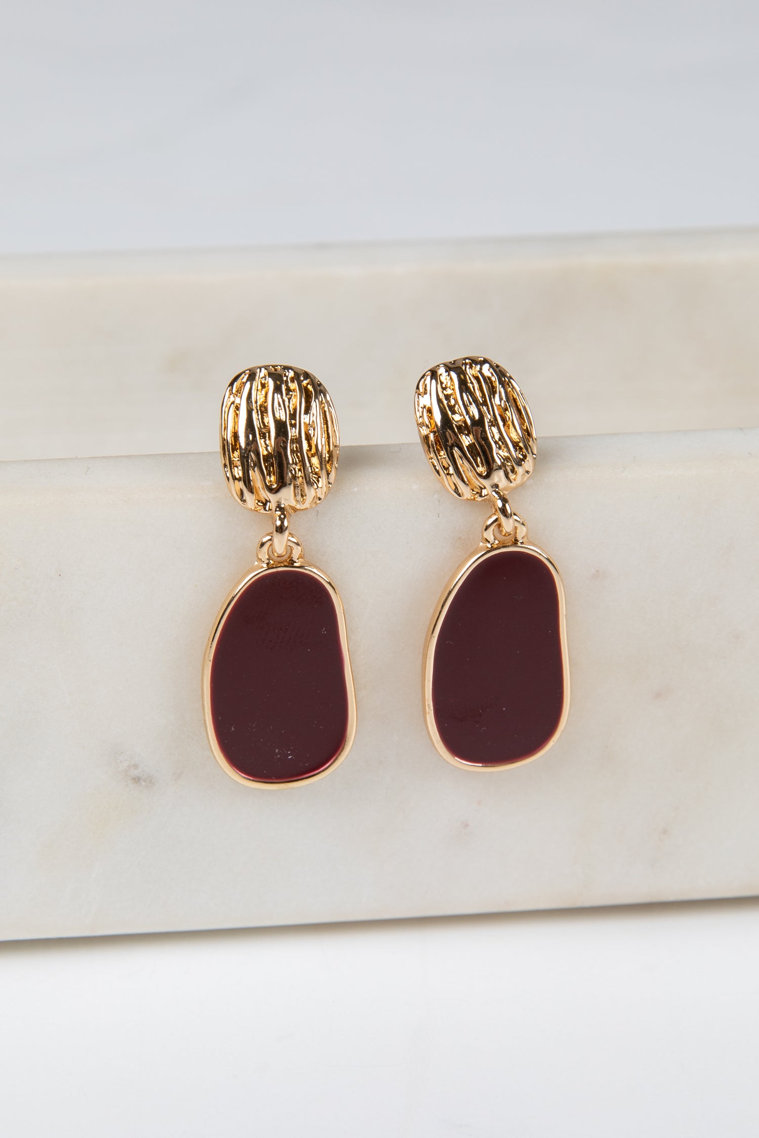 Gold and burgundy earrings on a marble surface