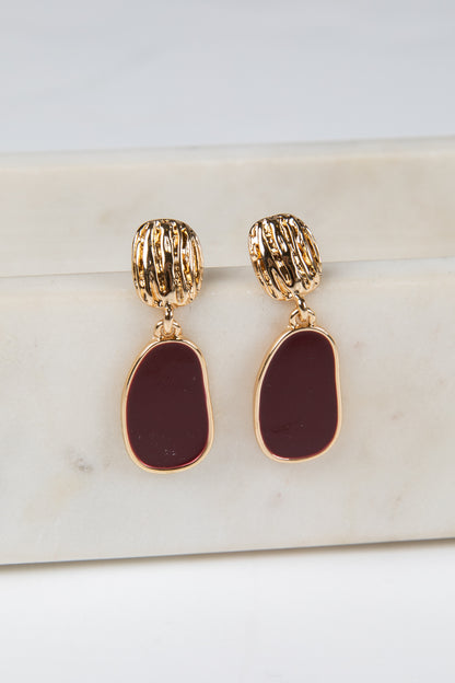 Gold and burgundy earrings on a marble surface