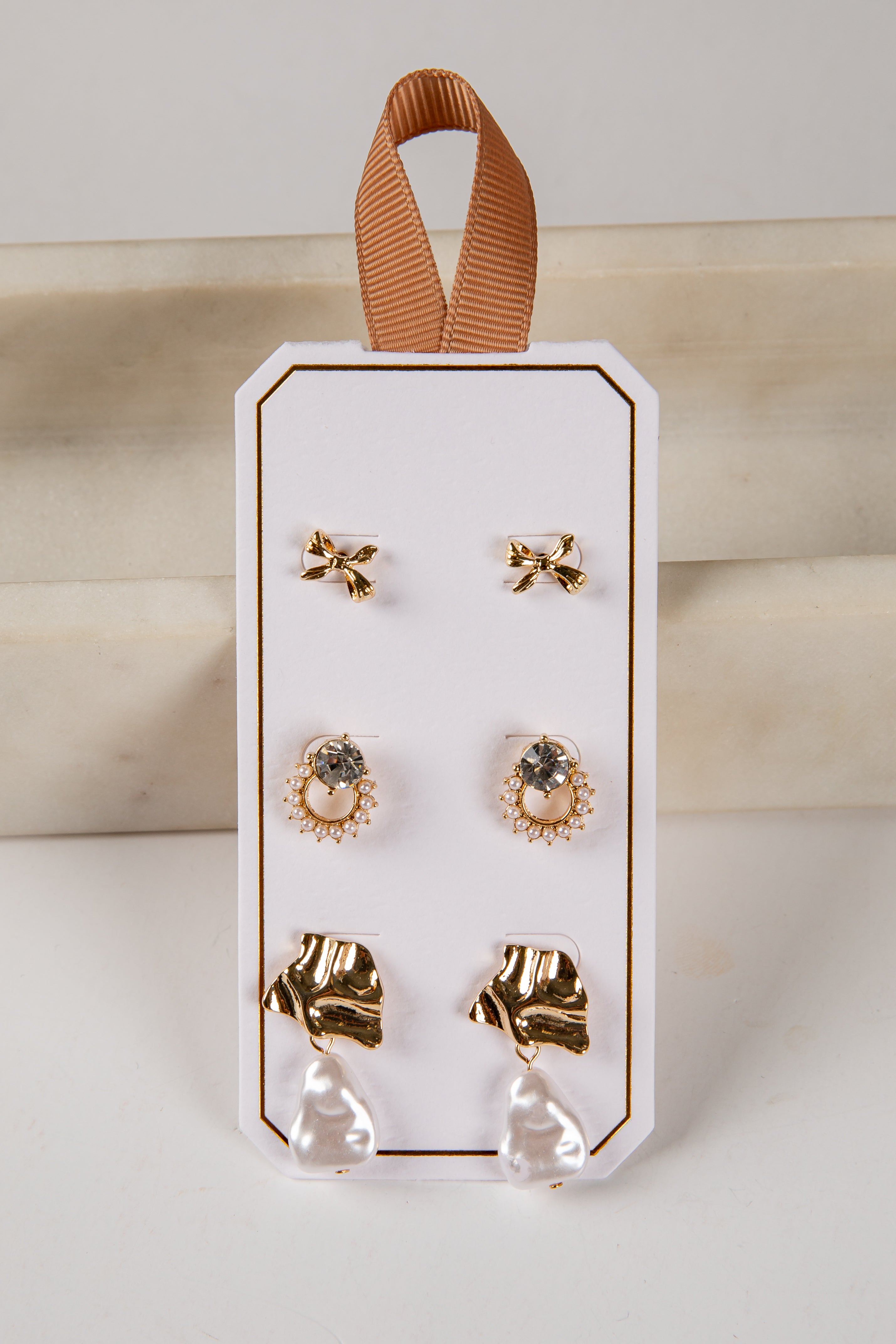 Set of earrings on a white card with a brown ribbon, against a light background