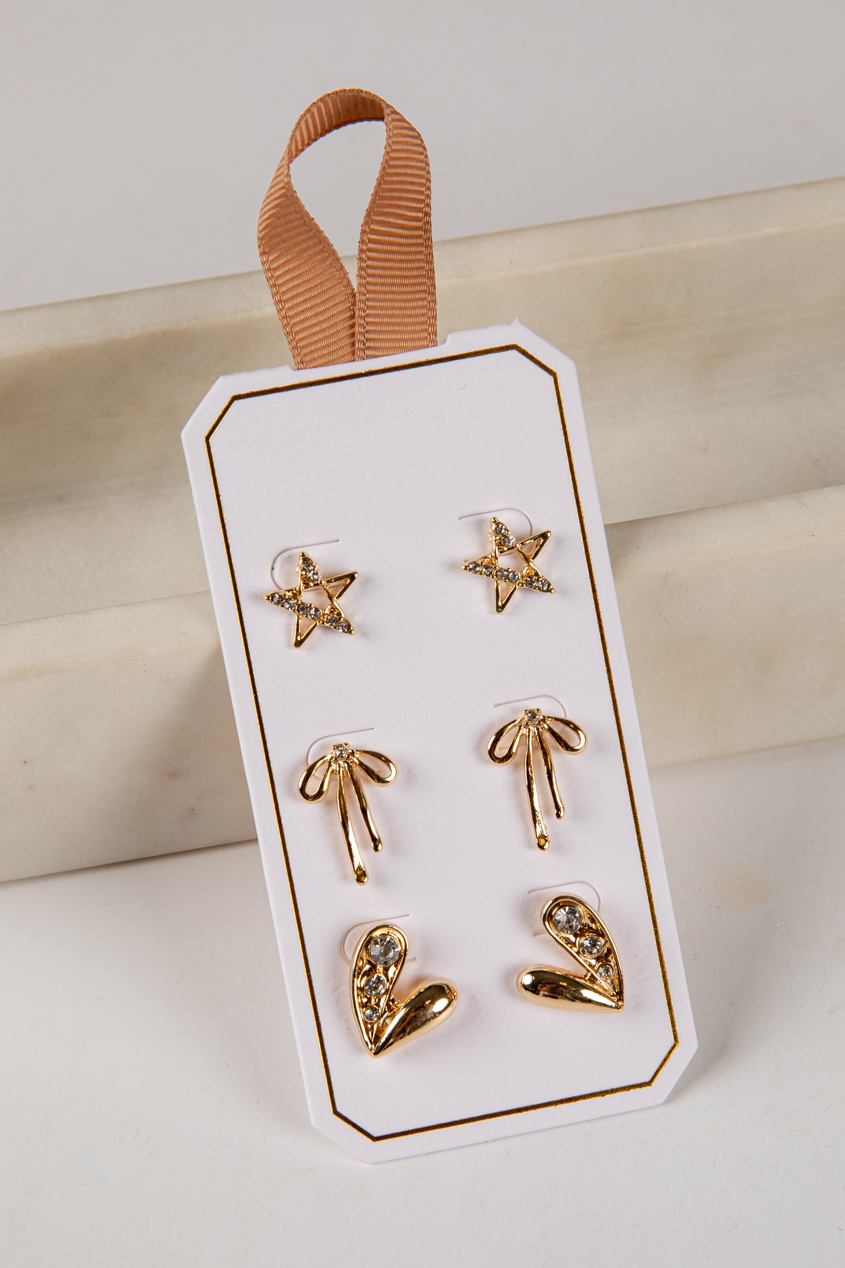 Set of gold earrings on a white card with a brown ribbon against a beige background