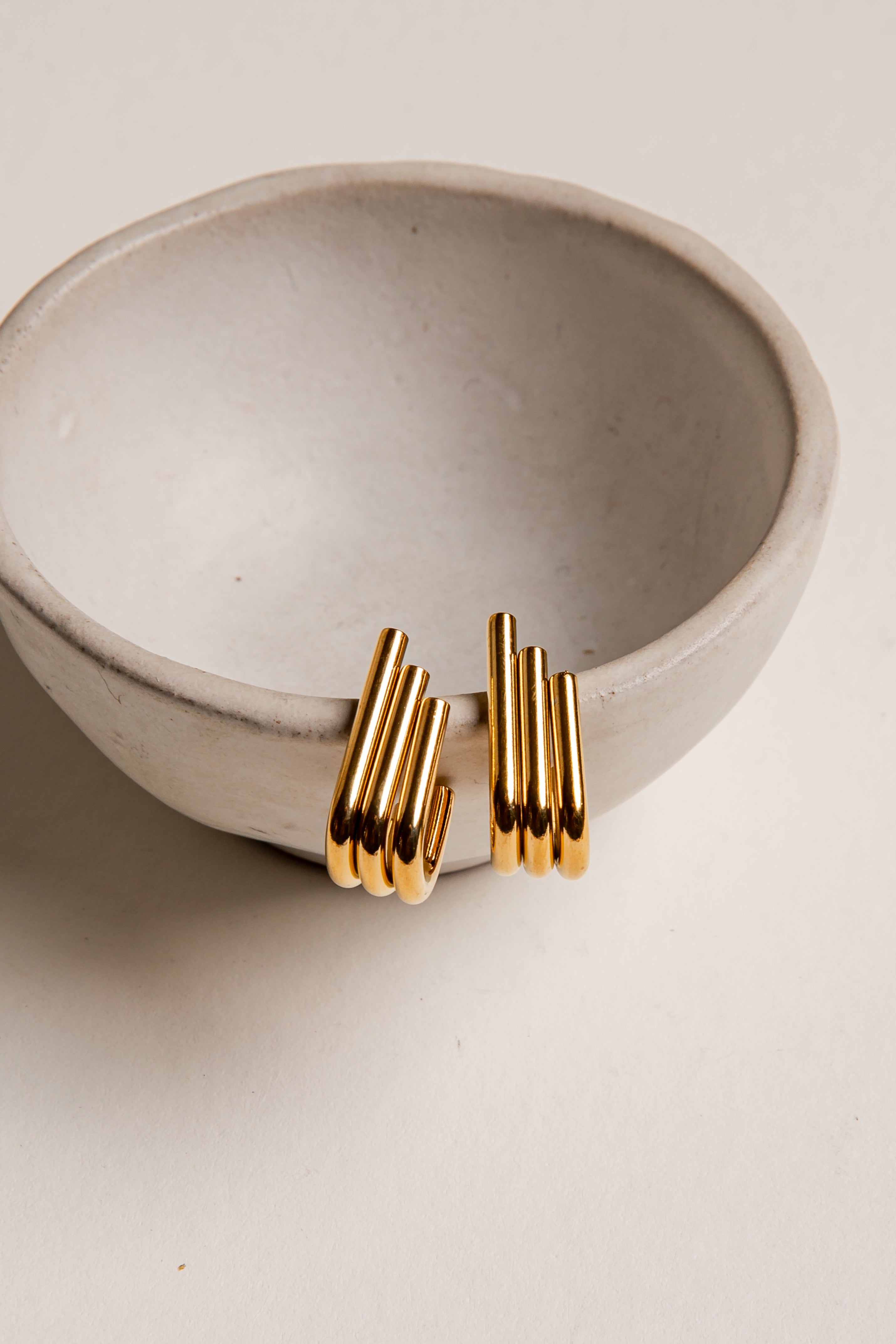 Gold earrings on a beige ceramic bowl