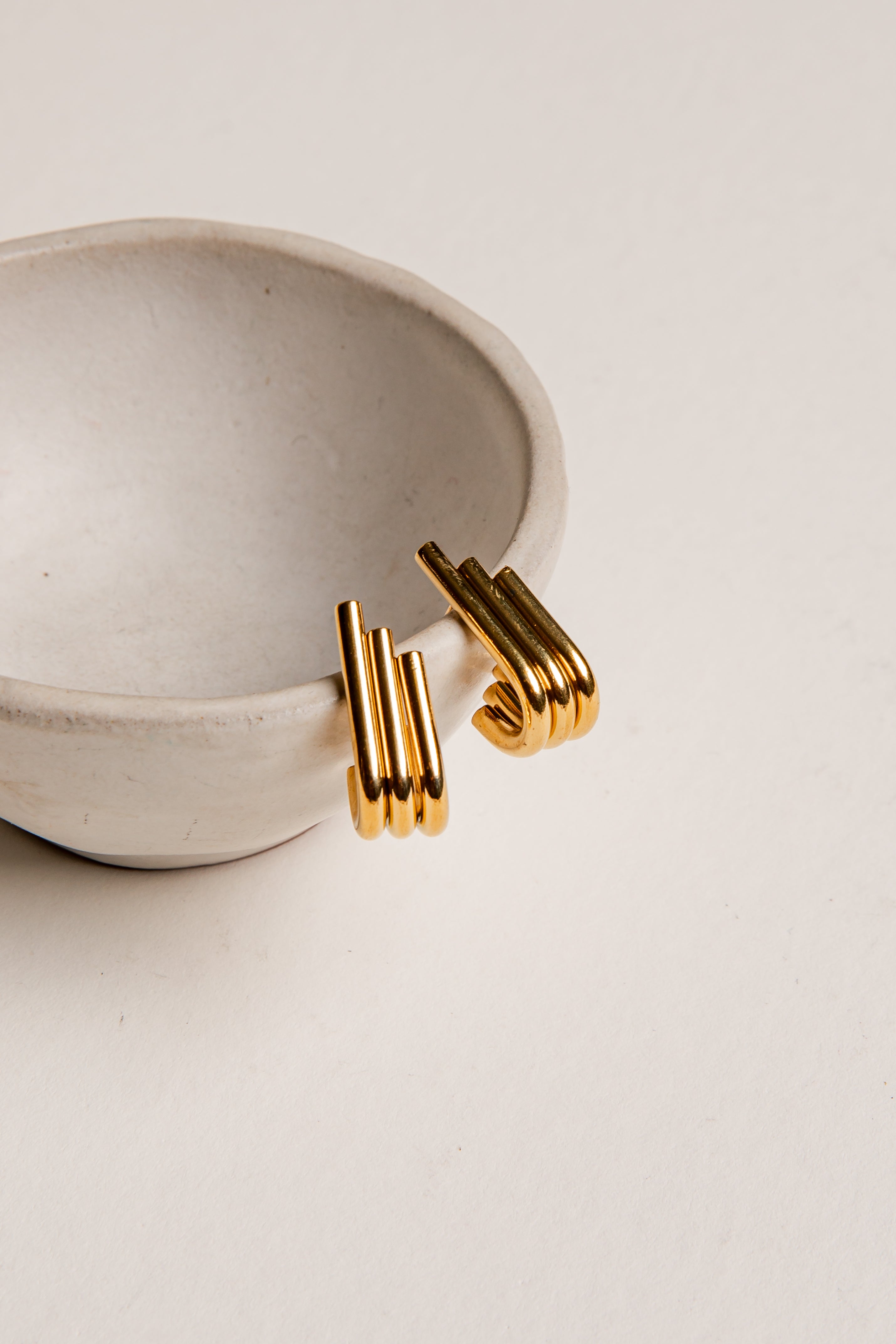 Gold hoop earrings on a beige surface with a ceramic dish