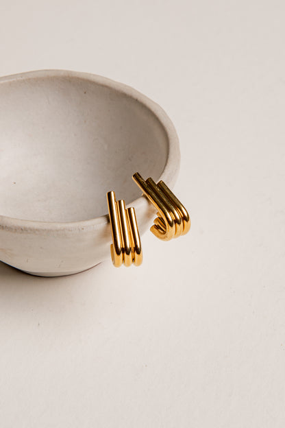 Gold hoop earrings on a beige surface with a ceramic dish