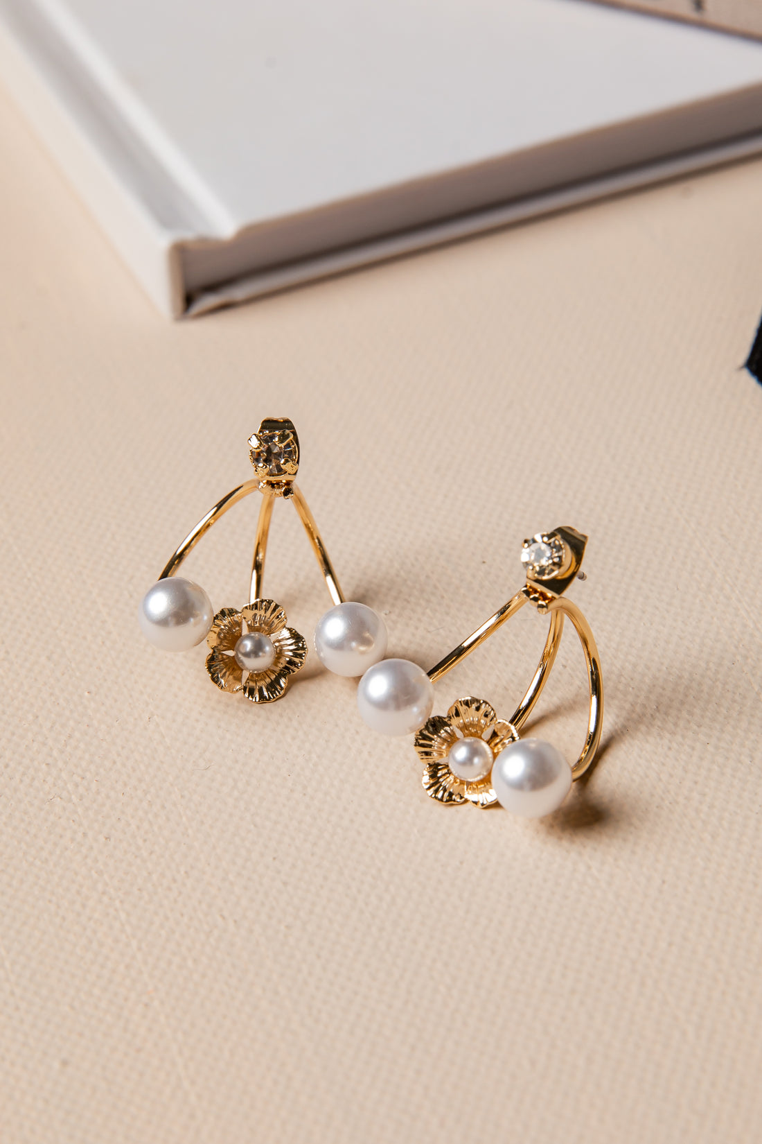 Gold earrings with pearls on a beige surface