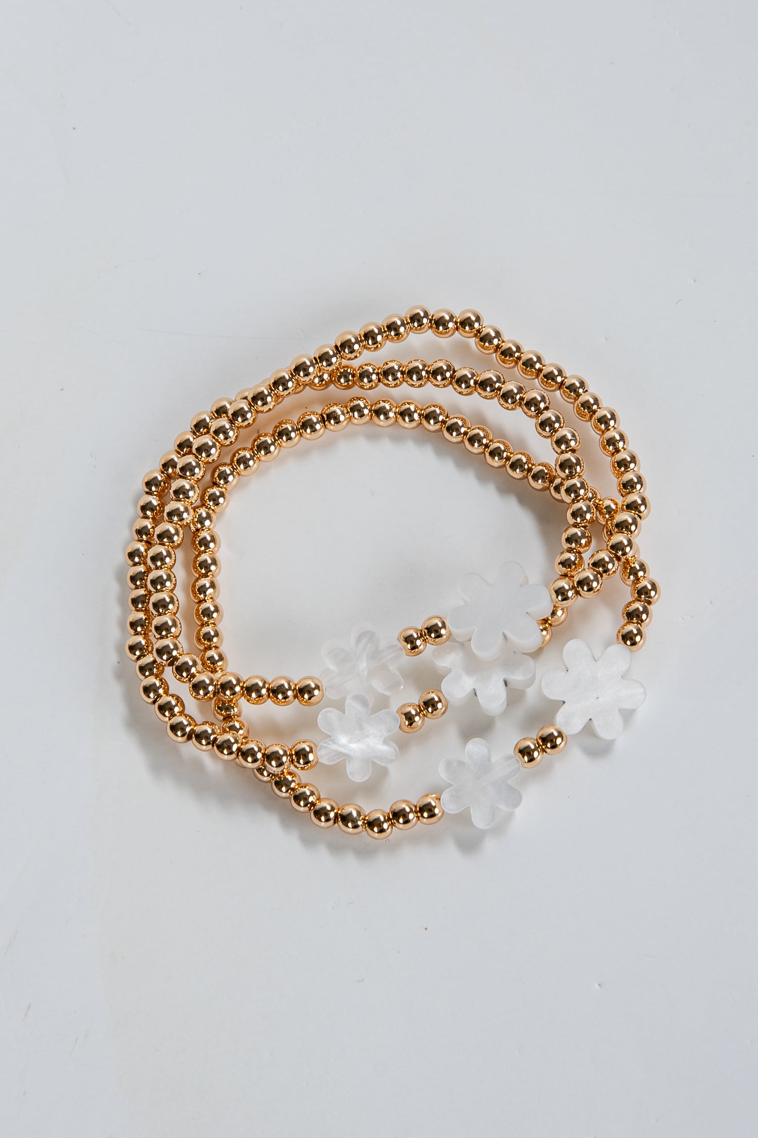 Gold beaded necklace with white floral pendants on a light gray background