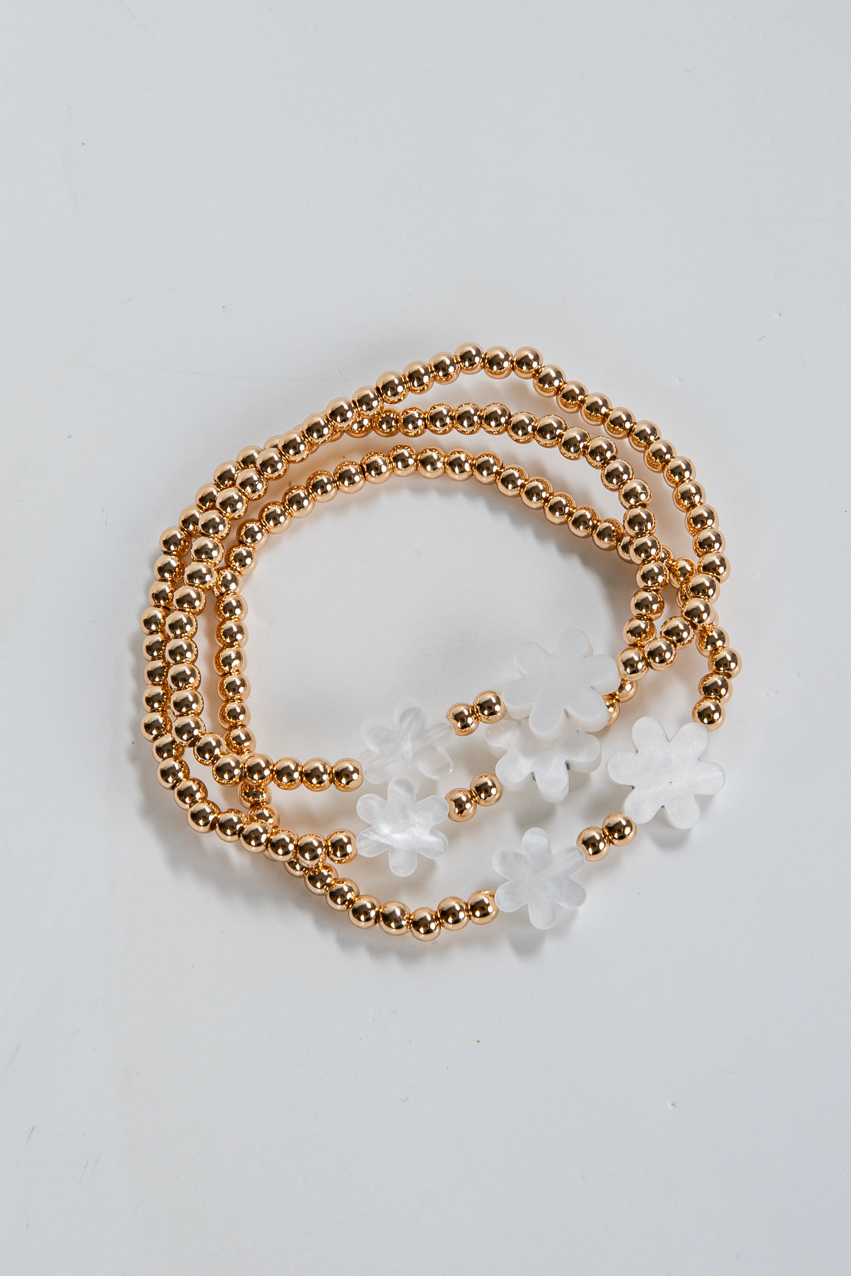 Gold beaded necklace with white floral pendants on a light gray background