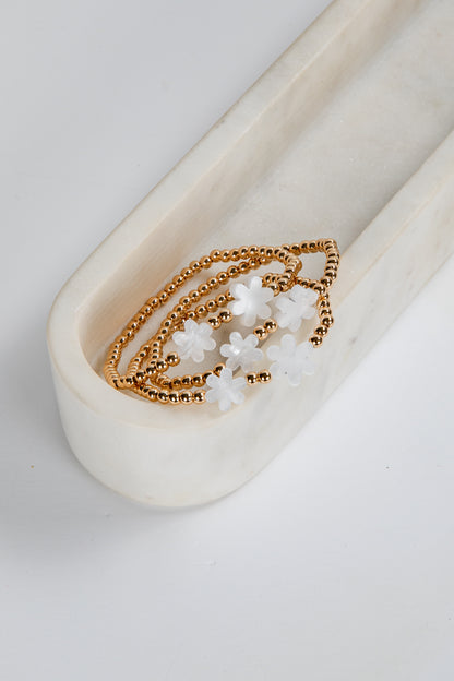 Gold bracelet with white beads on a white ceramic dish