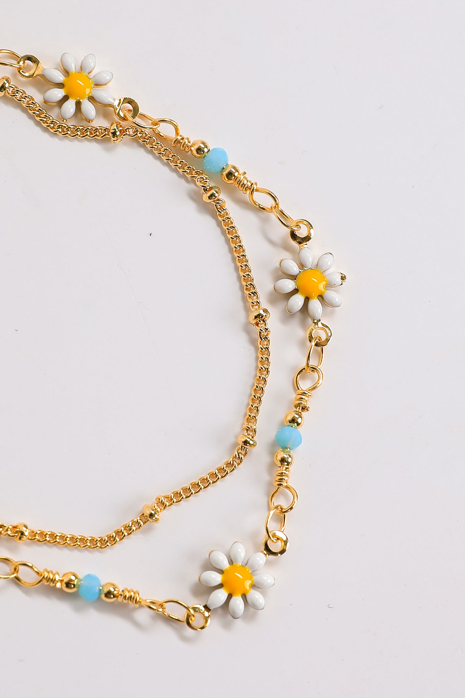 Gold chain necklace with daisy flower pendants on a light gray background