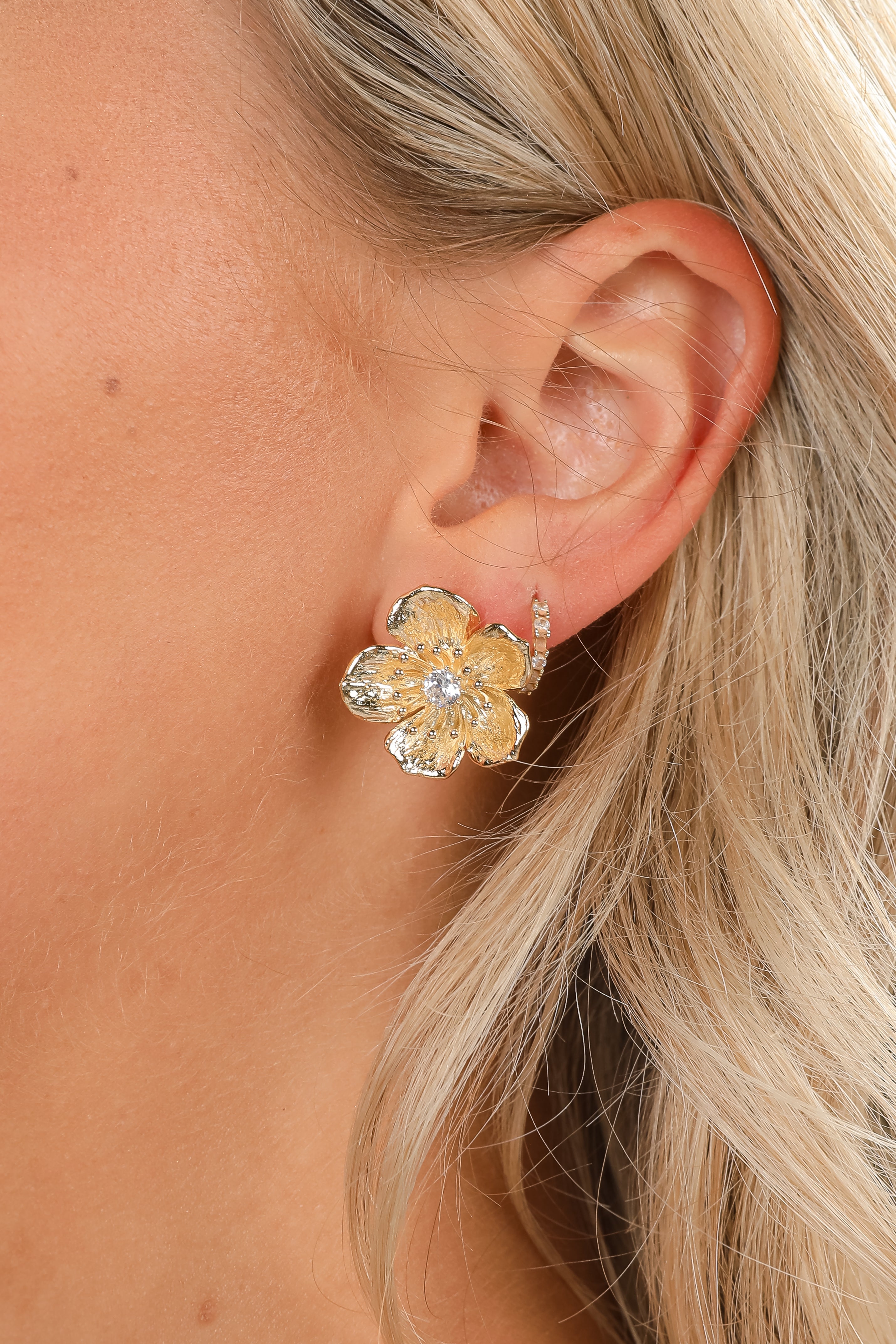 Close-up of a person wearing a gold flower-shaped earring.