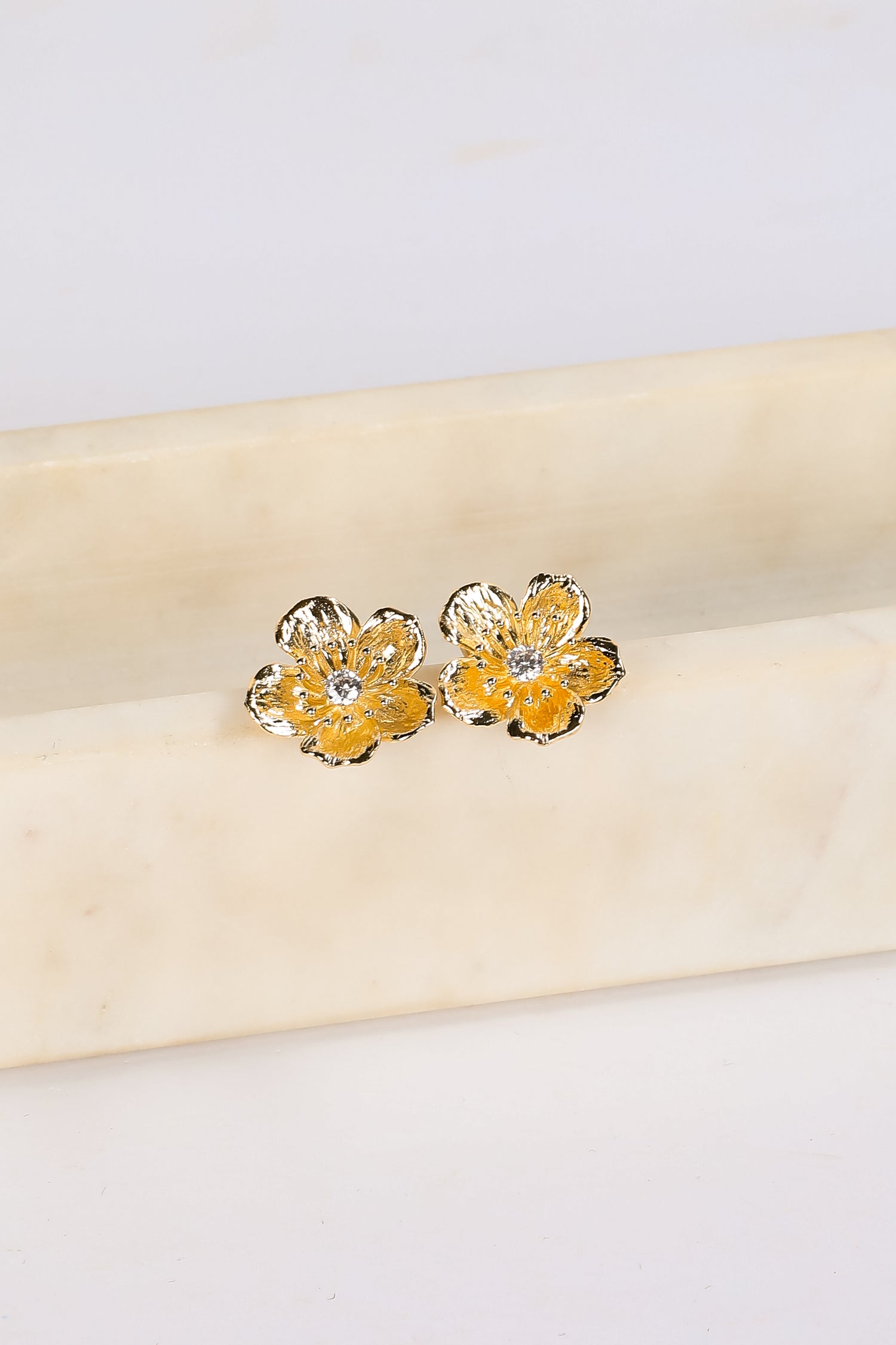 Gold flower-shaped earrings on a beige fabric background