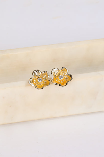 Gold flower-shaped earrings on a beige fabric background