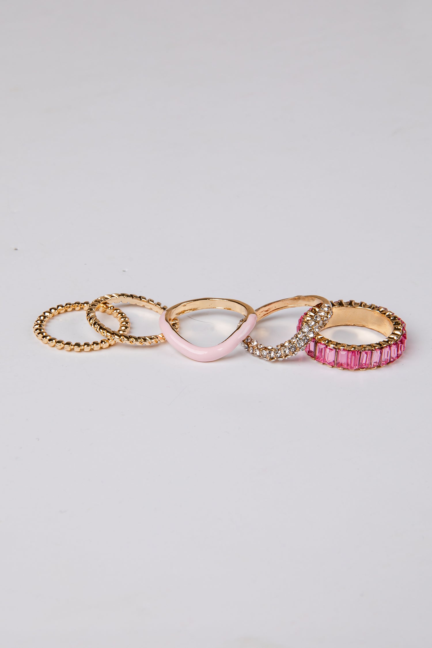Set of five gold and pink rings on a light gray background