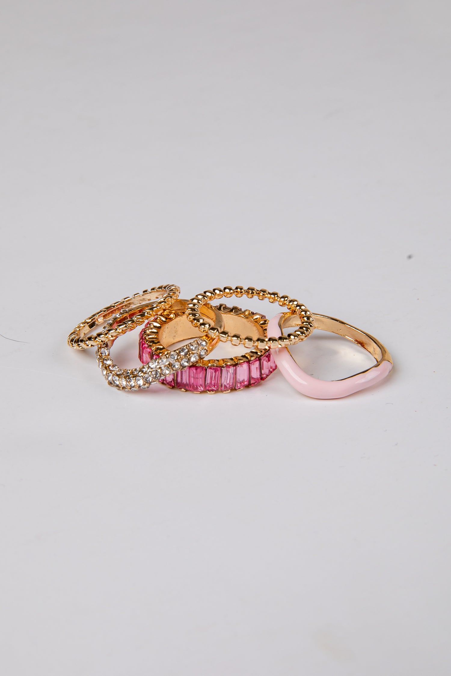 Three rings with gold, pink, and clear gemstone designs on a light gray background