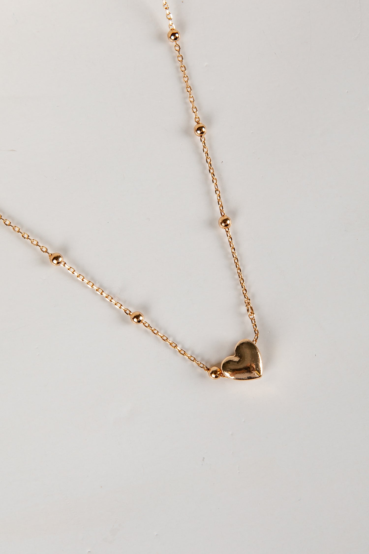 Gold heart-shaped pendant necklace on a light gray background