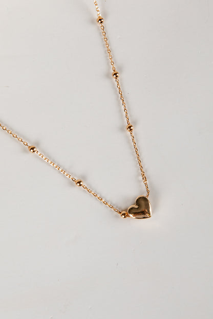 Gold heart-shaped pendant necklace on a light gray background