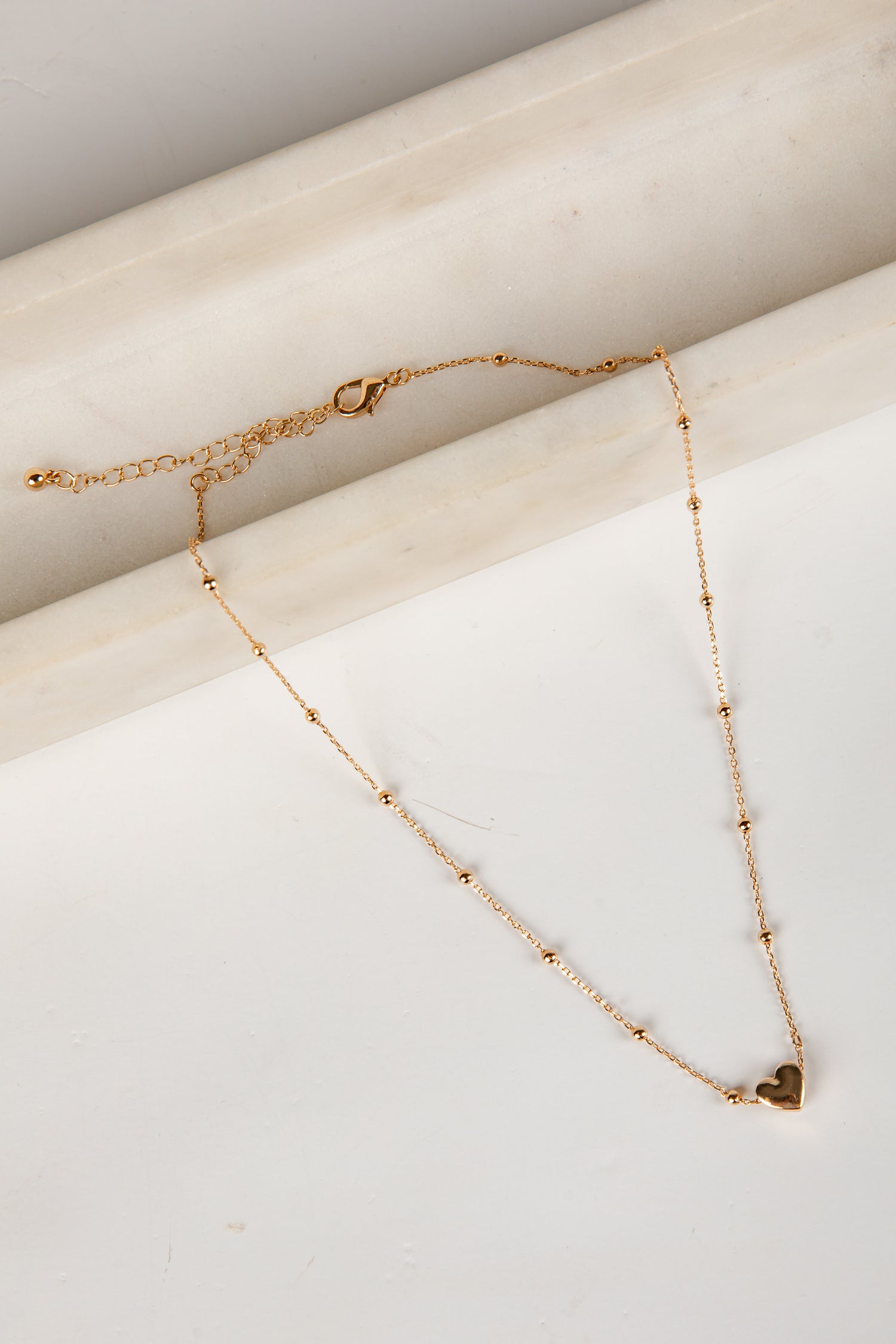 Gold necklace with a heart pendant on a marble surface