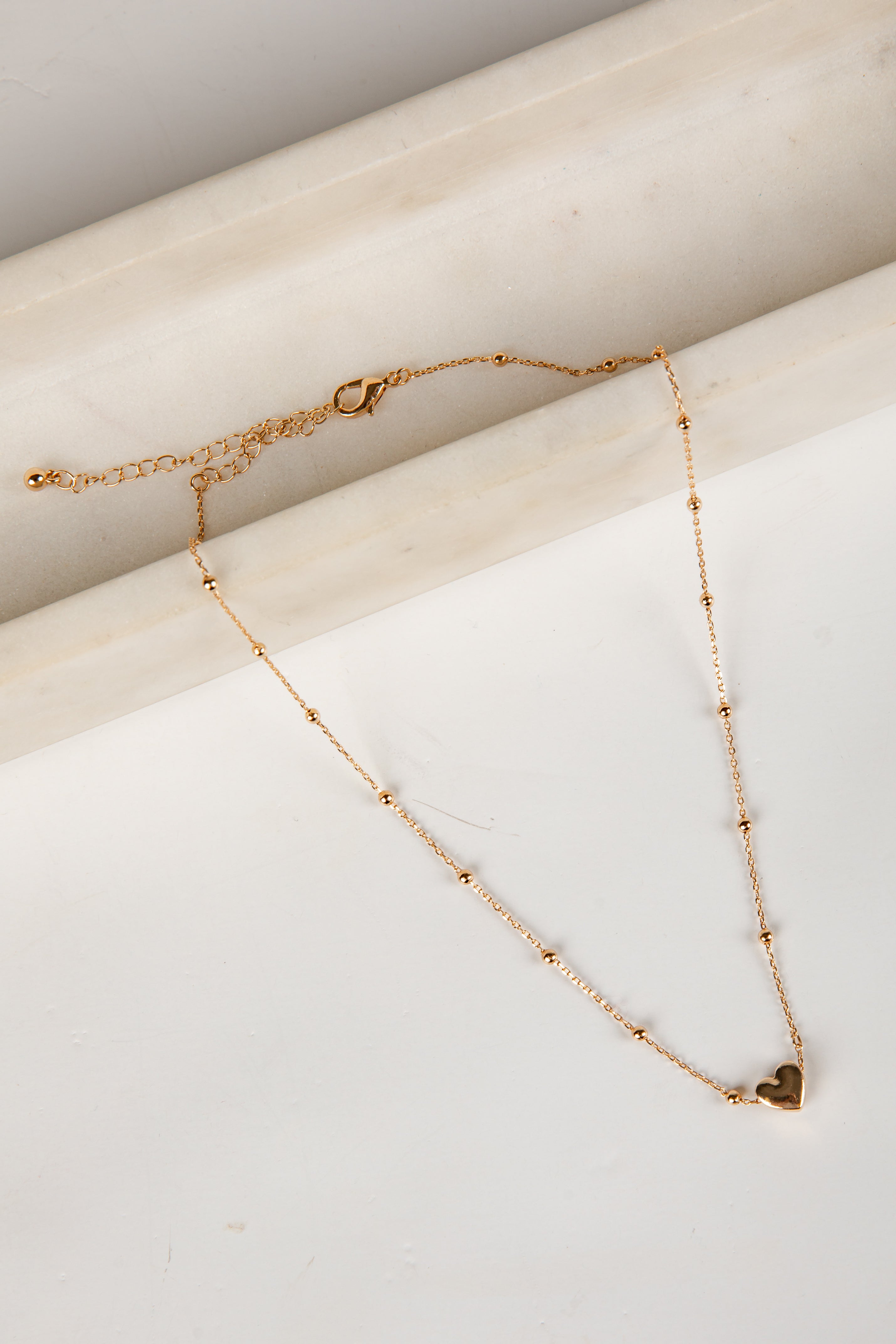 Gold necklace with a heart pendant on a marble surface