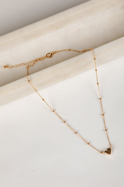 Gold necklace with a heart pendant on a marble surface